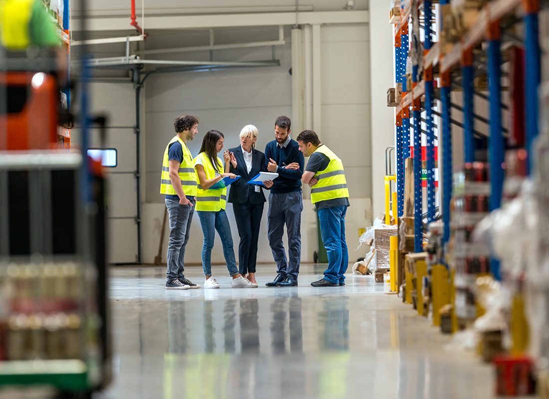 Business Insurance - View of Managers and Group of Employees Discussing Business Operations While Standing in a Warehouse with Stocked Shelves
